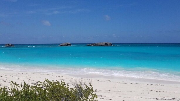 A beach with clear turquoise water, white sand, and a few rocks in the distance. - Three Sisters Villa (Mount Thompson)