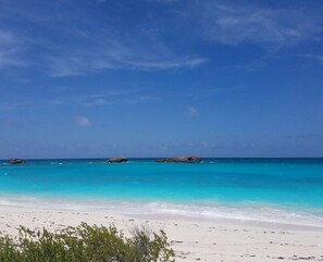 A beach with clear turquoise water, white sand, and a few rocks in the distance.