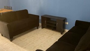 A living room with a blue wall, a black sofa, and a wooden table. - Three Sisters Villa (Mount Thompson)