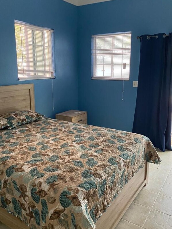 A bedroom with a bed, two windows, a nightstand, and a curtain.