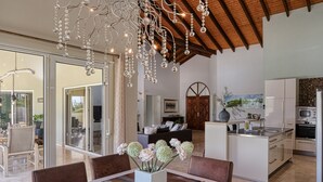 Una cocina moderna con electrodomésticos de acero inoxidable, un comedor con mesa y sillas de madera, y una lámpara de araña con detalles de cristal.