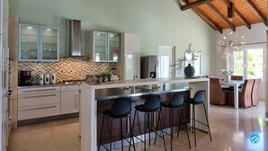 Una cocina moderna con una isla central, taburetes de bar y un comedor con candelabro.