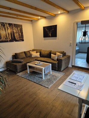 A modern living room with a wooden ceiling, a sectional sofa, a coffee table, and artwork on the walls. - Spessartbude Schollbrunn (Schollbrunn)