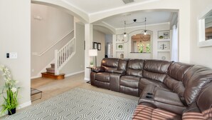 A spacious living room with a large leather sectional sofa, a staircase, and a chandelier. - The Secret Serenity Villa – 3 Miles from Disney, Endless Comfort & Fun (Kissimmee)