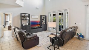 A spacious living room with a large flat-screen TV, leather recliners, a coffee table, and a ceiling fan. - The Secret Serenity Villa – 3 Miles from Disney, Endless Comfort & Fun (Kissimmee)
