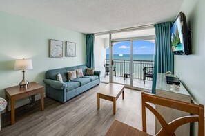 Relax in this stylish living room with a sofa, coffee table, and dining table, offering a view of the ocean from the balcony.