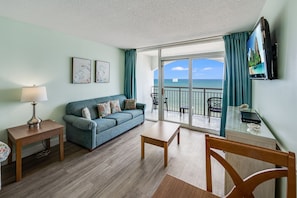 Relax in this stylish living room with a sofa, coffee table, and dining table, offering a view of the ocean from the balcony.