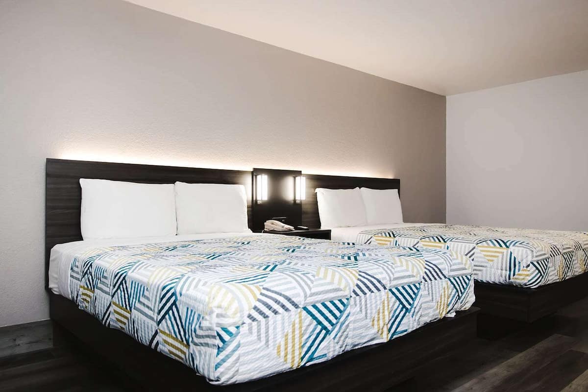 A hotel room with two beds, each with a patterned bedspread, a dark headboard, and a bedside table with a lamp.