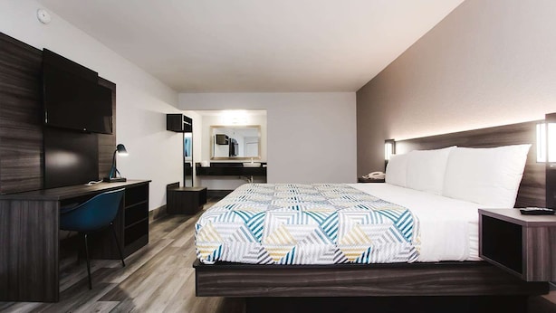 Ein Hotelzimmer mit einem großen Bett, einem Schreibtisch mit Stuhl, einem Spiegel und einem Nachttisch mit Lampe.