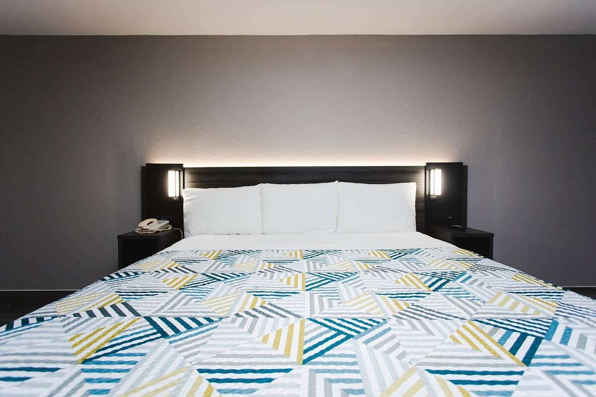 A hotel room with a bed, a nightstand, a telephone, and a wall-mounted light fixture.