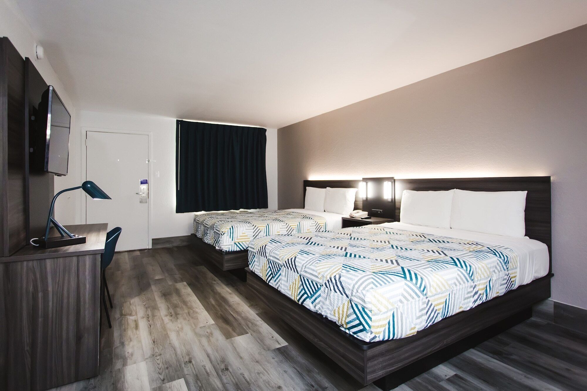 Ett hotellrum med en säng, sängbord, ett skrivbord med en lampa och en spegel.
