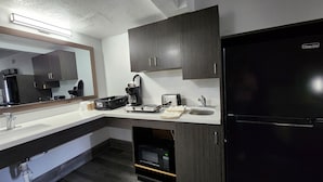 Eine moderne Küche mit dunklen Holzschränken, einem schwarzen Kühlschrank, einer Mikrowelle, einer Kaffeemaschine und einem Toaster.