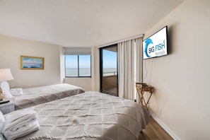 Quarto de hotel com duas camas, televisão, um quadro e vista para o mar.