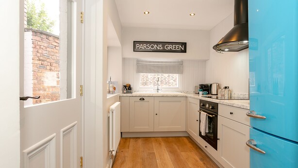 A kitchen with white cabinets, a blue refrigerator, and a window with a view of the outside. - Central Harrogate 2 Bed Victorian Terrace (Harrogate)