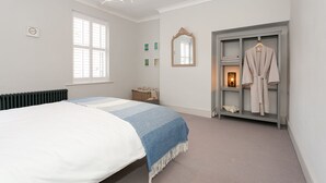 A bedroom with a bed, a window, a mirror, a robe rack, and a small bedside table. - Central Harrogate 2 Bed Victorian Terrace (Harrogate)
