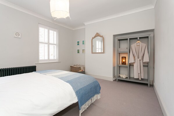 Une chambre à coucher comprenant un lit, une fenêtre, un miroir, un porte-manteau et une petite table de chevet.