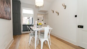 A dining area with a white table and chairs, a hanging light fixture, and a view through a window. - Central Harrogate 2 Bed Victorian Terrace (Harrogate)