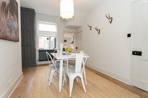Un coin repas avec une table et des chaises blanches, un luminaire suspendu et une vue par la fenêtre.