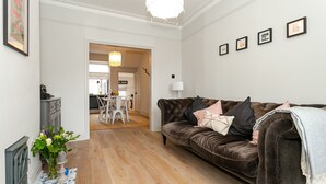 A living room with a brown leather sofa, a vase with flowers, and a tiled floor. - Central Harrogate 2 Bed Victorian Terrace (Harrogate)
