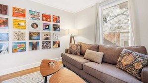 Un soggiorno con un divano marrone, cuscini decorati, un piccolo tavolino in legno e una parete decorata con diversi poster.