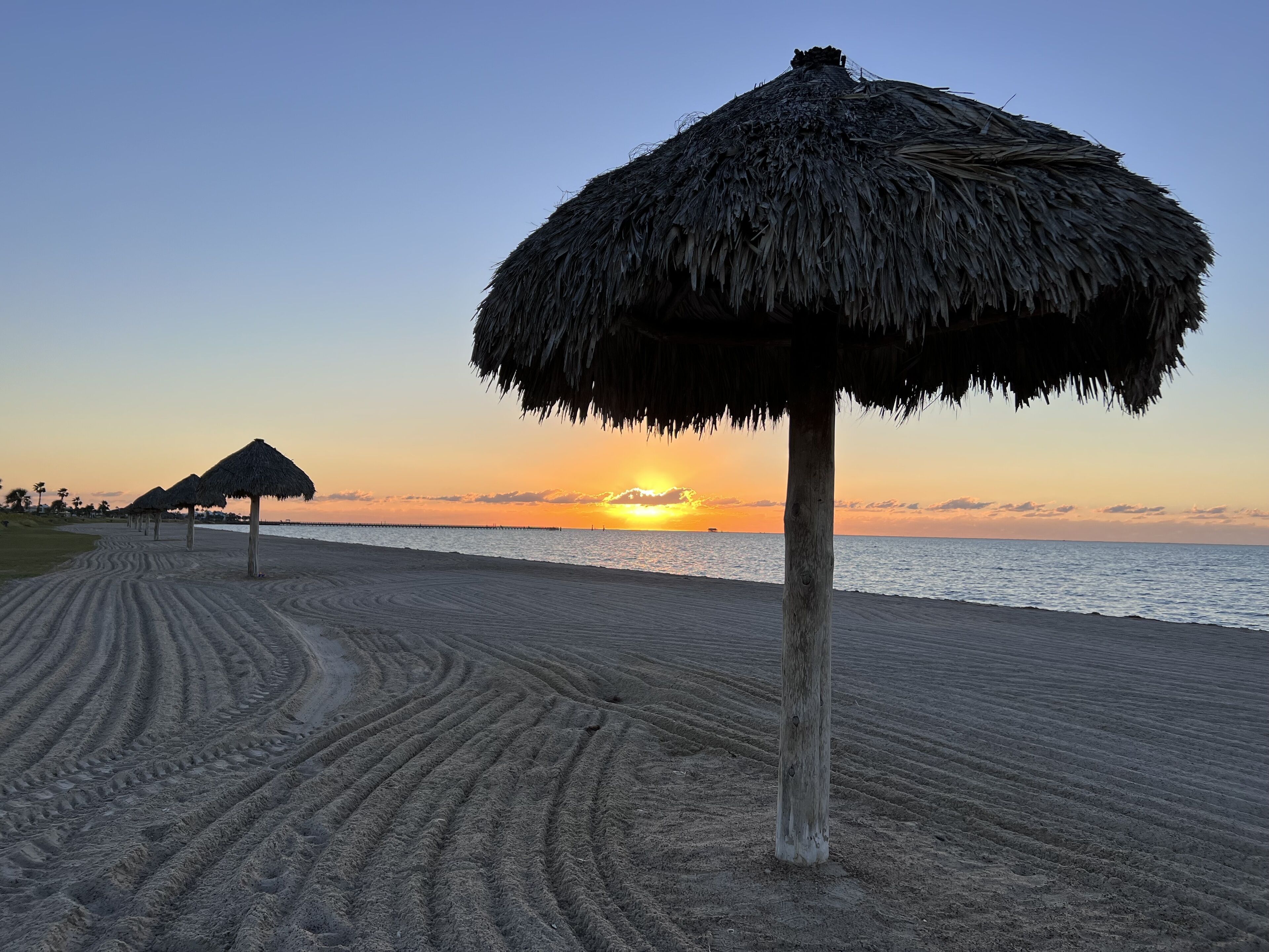 Une plage avec un parasol en chaume et un poteau en bois.