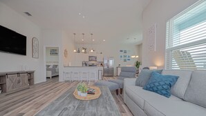 Ein modernes Wohnzimmer mit einem grauen Sofa, einem Couchtisch mit einer Pflanze und einer Küche im Hintergrund.