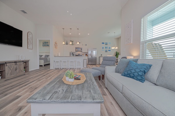 A modern living room with a grey sofa, a coffee table with a plant, and a kitchen in the background.