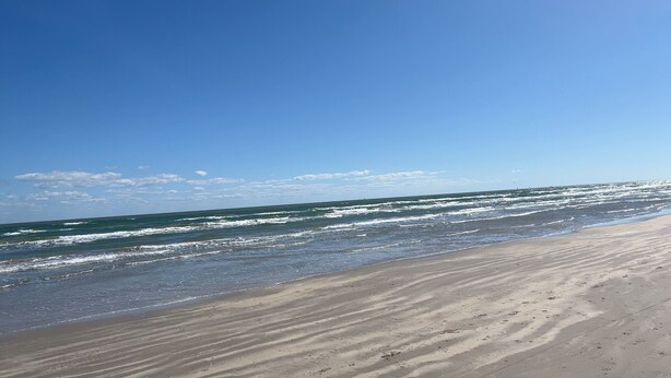 Ein Strand mit breitem Sandufer und sanften Wellen.