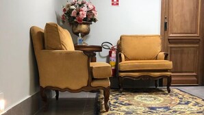 Un vestíbulo con dos sillones, un jarrón de flores, un extintor y una puerta que indica 'SAÍDA'.
