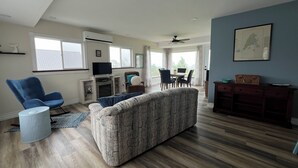 A spacious living room with a large couch, a blue armchair, and a dining area with a table and chairs. - Fantastic Beach & Ocean Views (Grand Manan)