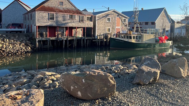 A waterfront building with a dock, a boat moored nearby, and a pile of rocks in the foreground. - Fantastic Beach & Ocean Views (Grand Manan)