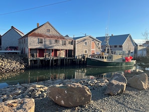 Un edificio frente al agua con un muelle, una embarcación amarrada cerca y un montón de rocas al frente.