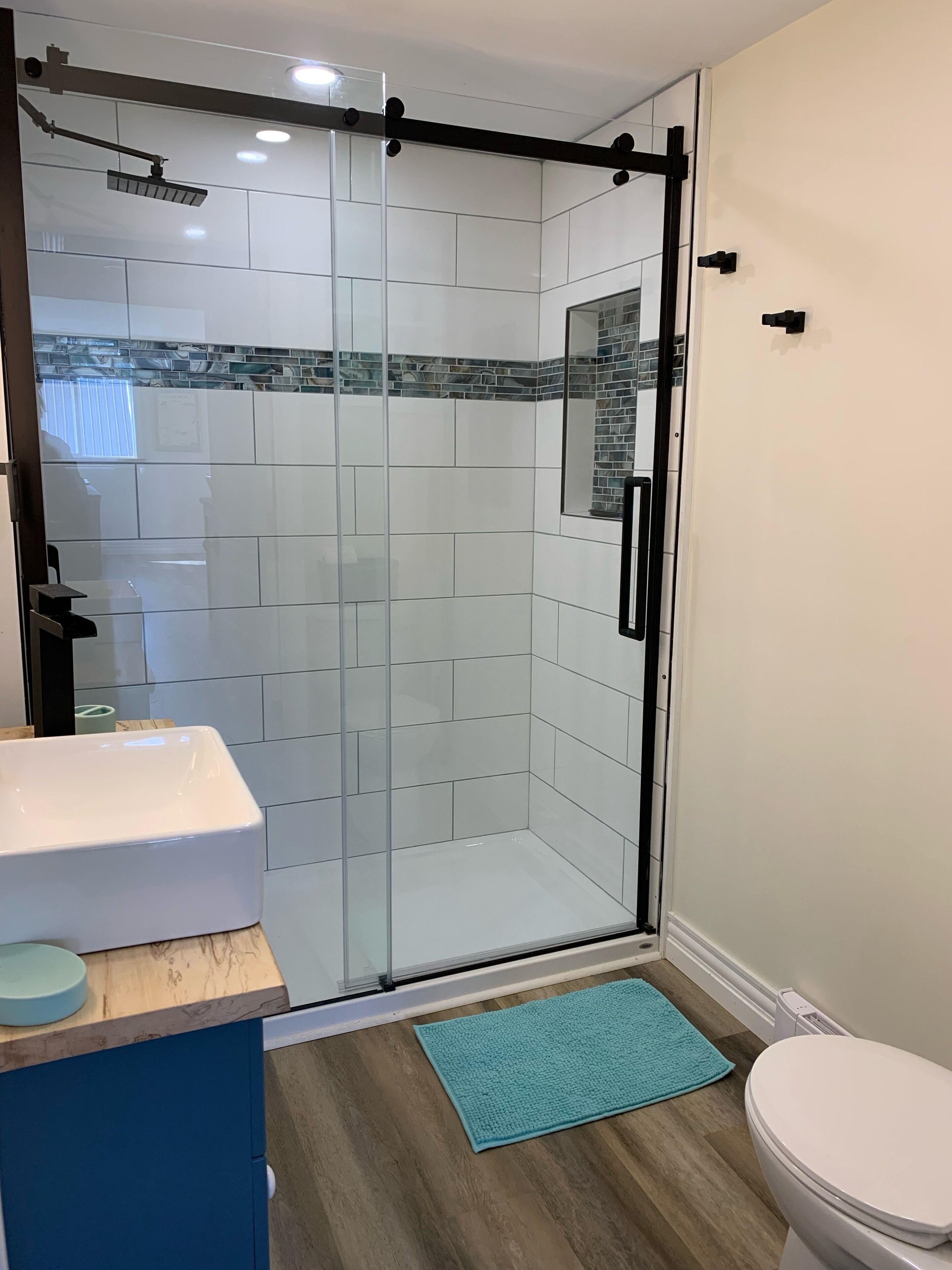 A modern bathroom with a glass shower enclosure, a white sink, and a blue mat.