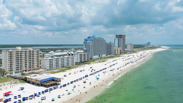 Ein Hotel direkt am Strand mit mehreren Gebäuden, einem weiten Sandstrand und einem Steg im Hintergrund.