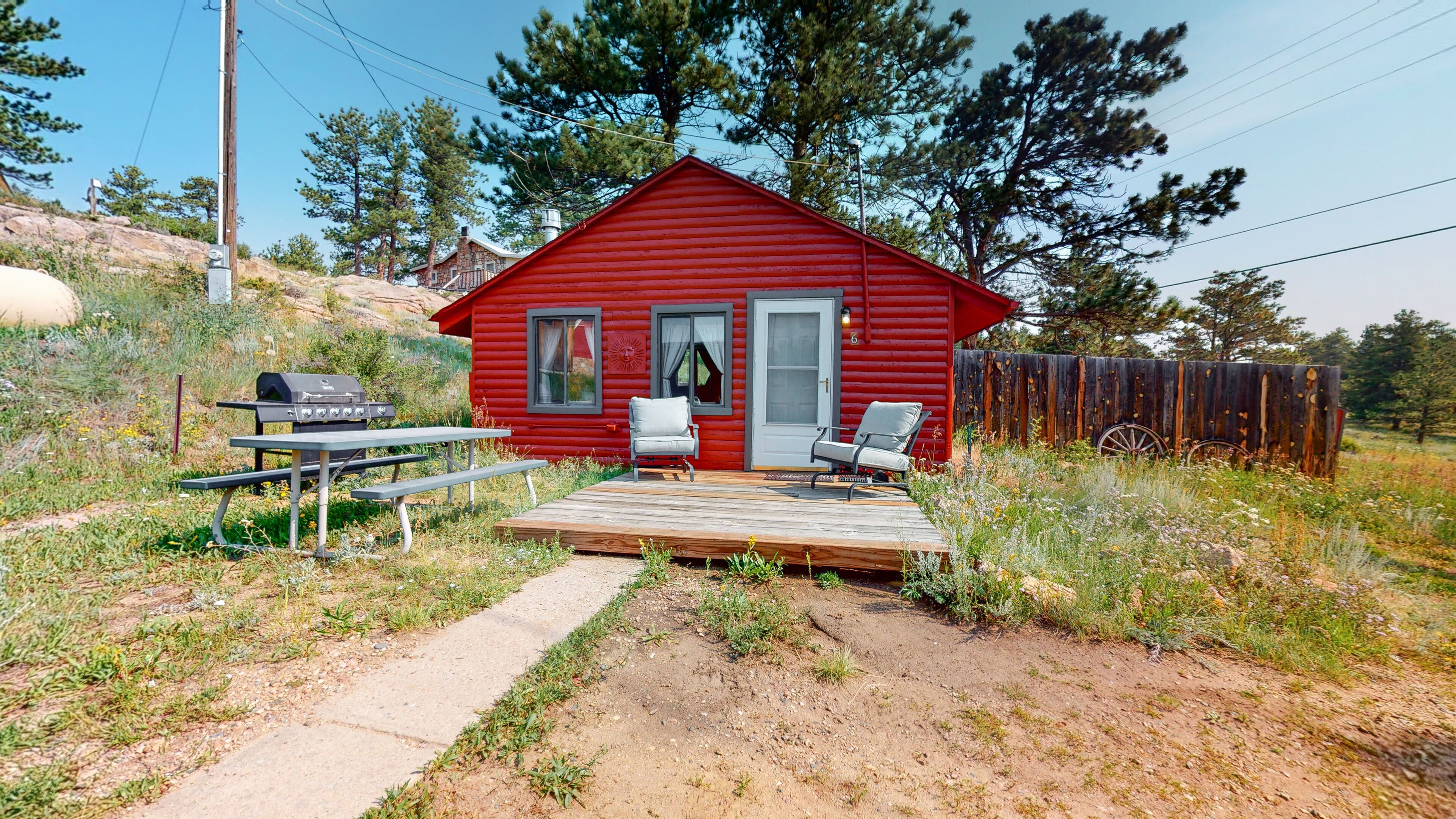 A red cabin with a wooden deck, two chairs, a table, and a grill.