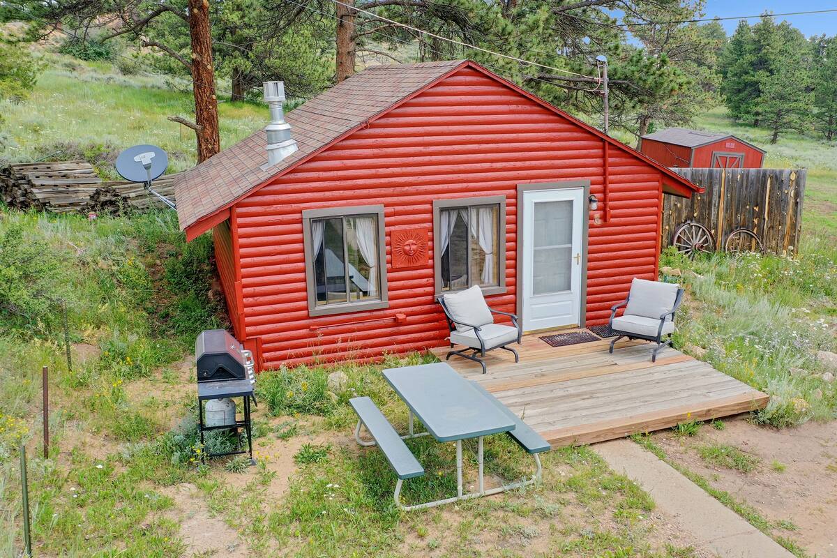 A red log cabin with two chairs and a picnic table outside.