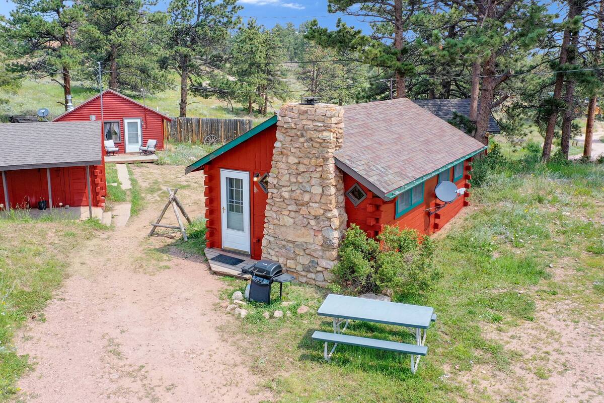 A red cabin with a stone chimney, a wooden deck, and a picnic table.
