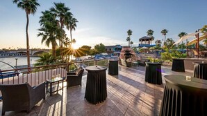 Una terraza con asientos al aire libre, vista al río y palmeras.
