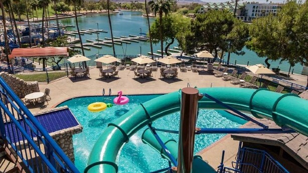 Zona de piscina con tobogán de agua, sillas de descanso y vistas al puerto deportivo.
