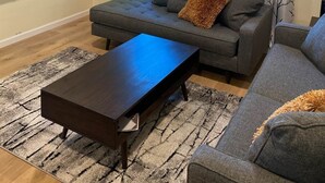 Una sala de estar con un sofá gris, una mesa de centro de madera y un televisor montado en la pared.