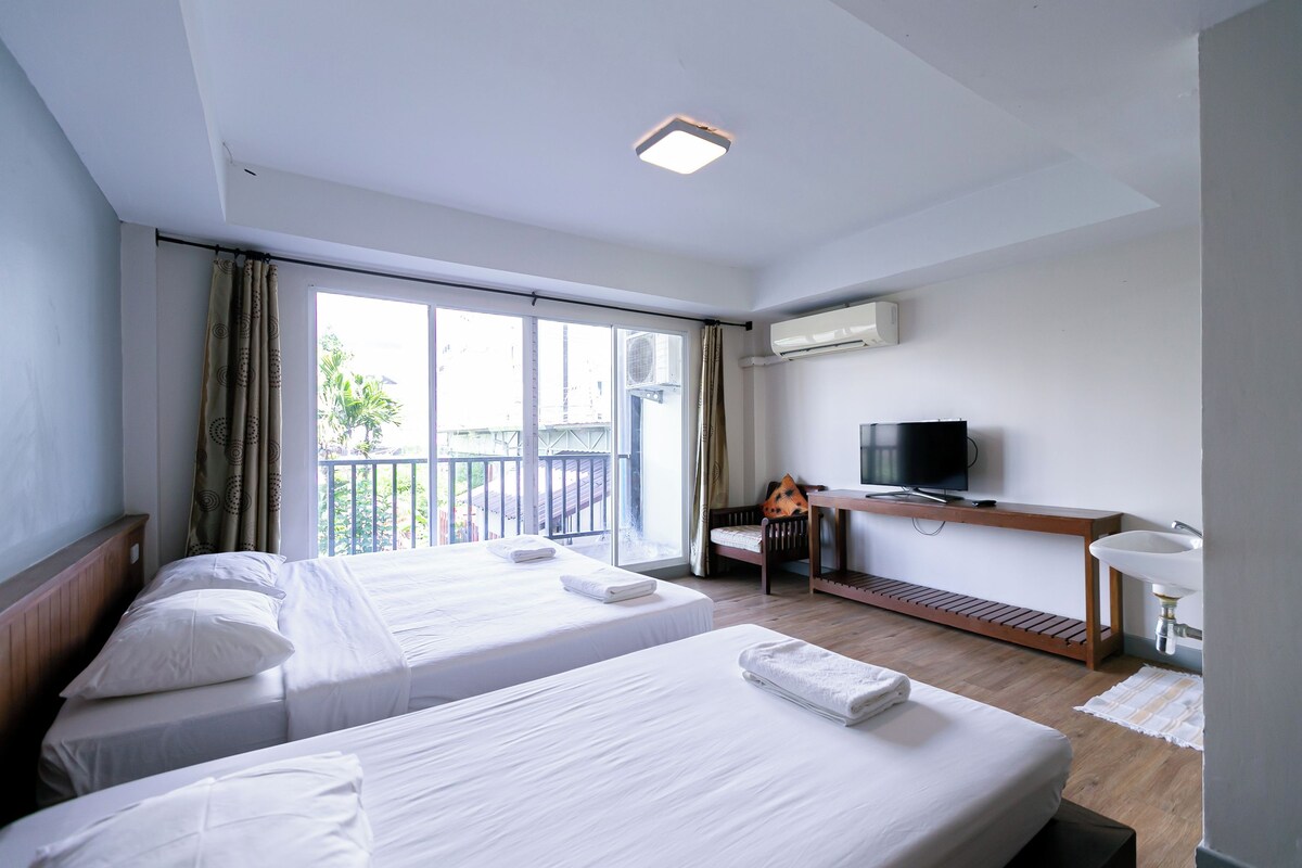 Una habitación de hotel con dos camas, un televisor, un equipo de aire acondicionado y un balcón con cortinas.