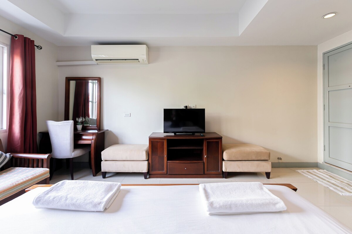 Habitación de hotel con cama, escritorio, silla, televisor y aire acondicionado.