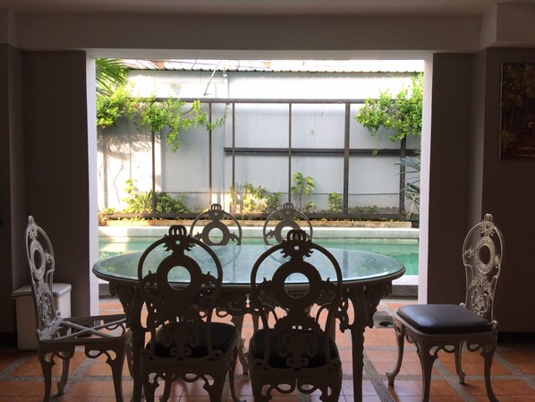 Un comedor con una mesa redonda y sillas ornamentadas, vista a una piscina y piso de baldosas.