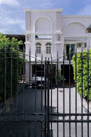 Une entrée fermée par un portail m ène à un immeuble à la façade blanche, doté d’une allée couverte et abritant un véhicule stationné à l’intérieur.