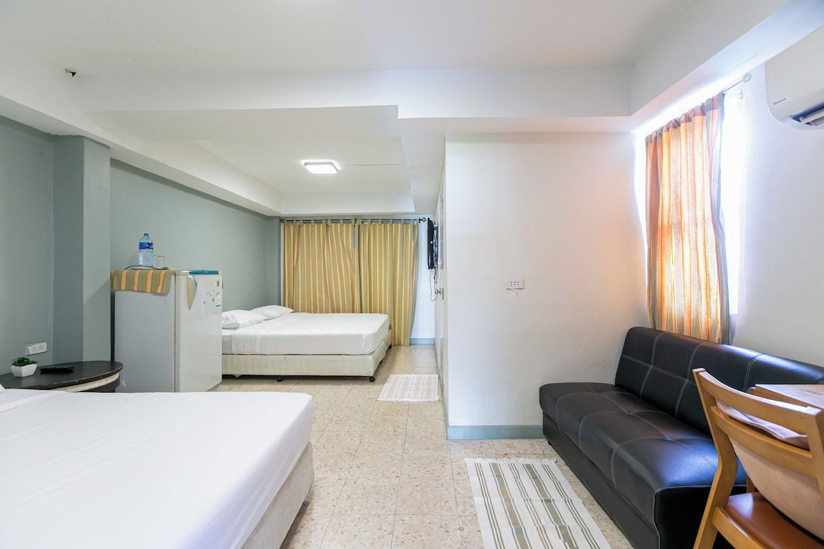 A hotel room with a bed, a desk with a water bottle, a sofa, and a window with curtains.