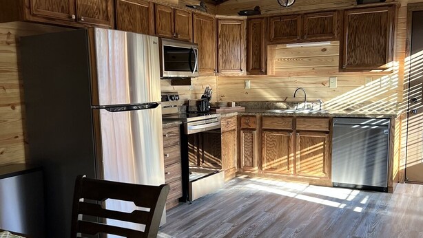A modern kitchen with wooden cabinetry, stainless steel appliances, and a dining area with a table and chairs.