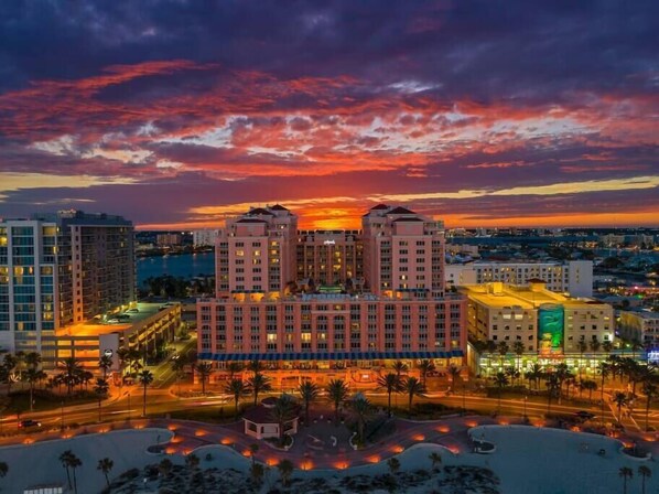 A hotel with a central courtyard, surrounded by palm trees and a view of the city skyline at sunset.