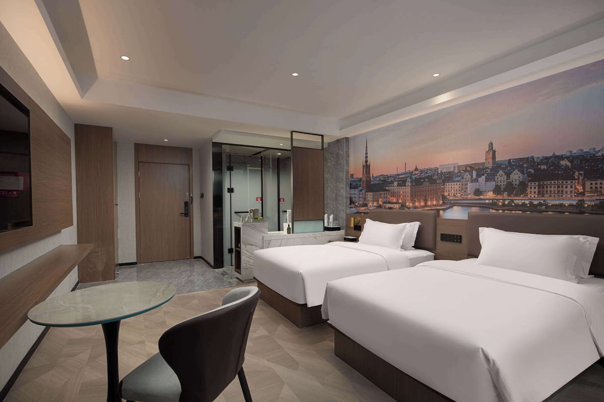 A hotel room with two beds, a glass table, a chair, and a cityscape view.