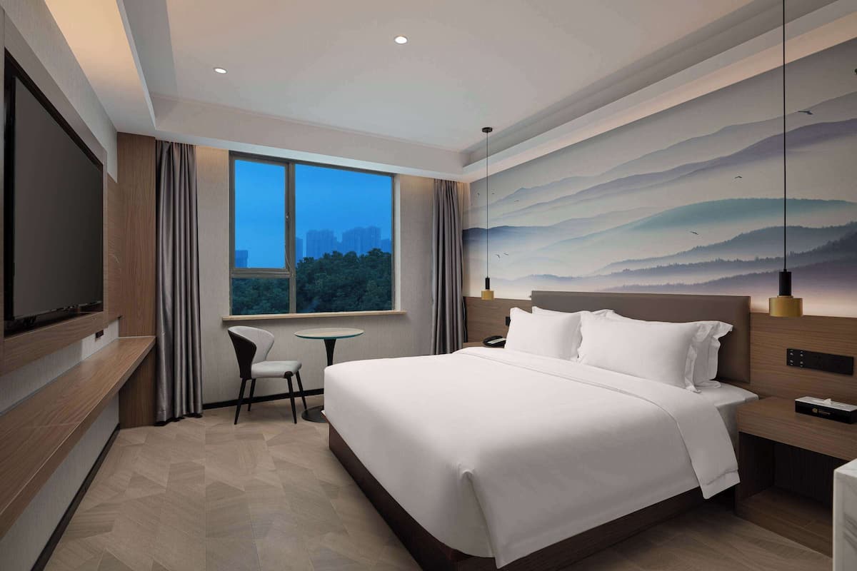 A modern hotel room with a large bed, a flat-screen TV, a small table, and a chair.