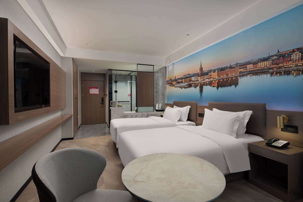 A hotel room with two beds, a TV, a desk with a phone, a chair, and a round table.